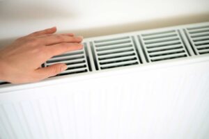 persona calentando su mano en un radiador con calefacción