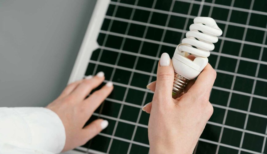 Mano sujetando una bombilla con un panel de energía solar de fondo