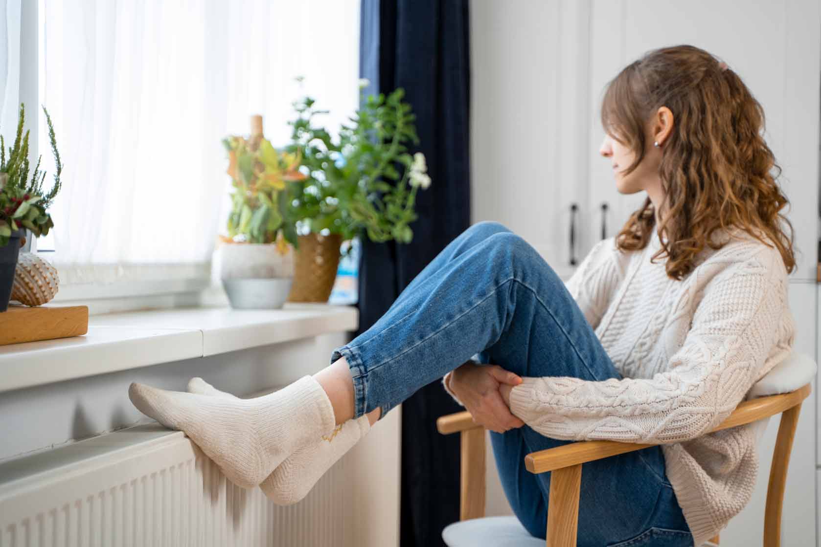 Mujer sentada mirando por la ventana con pies sobre el radiador